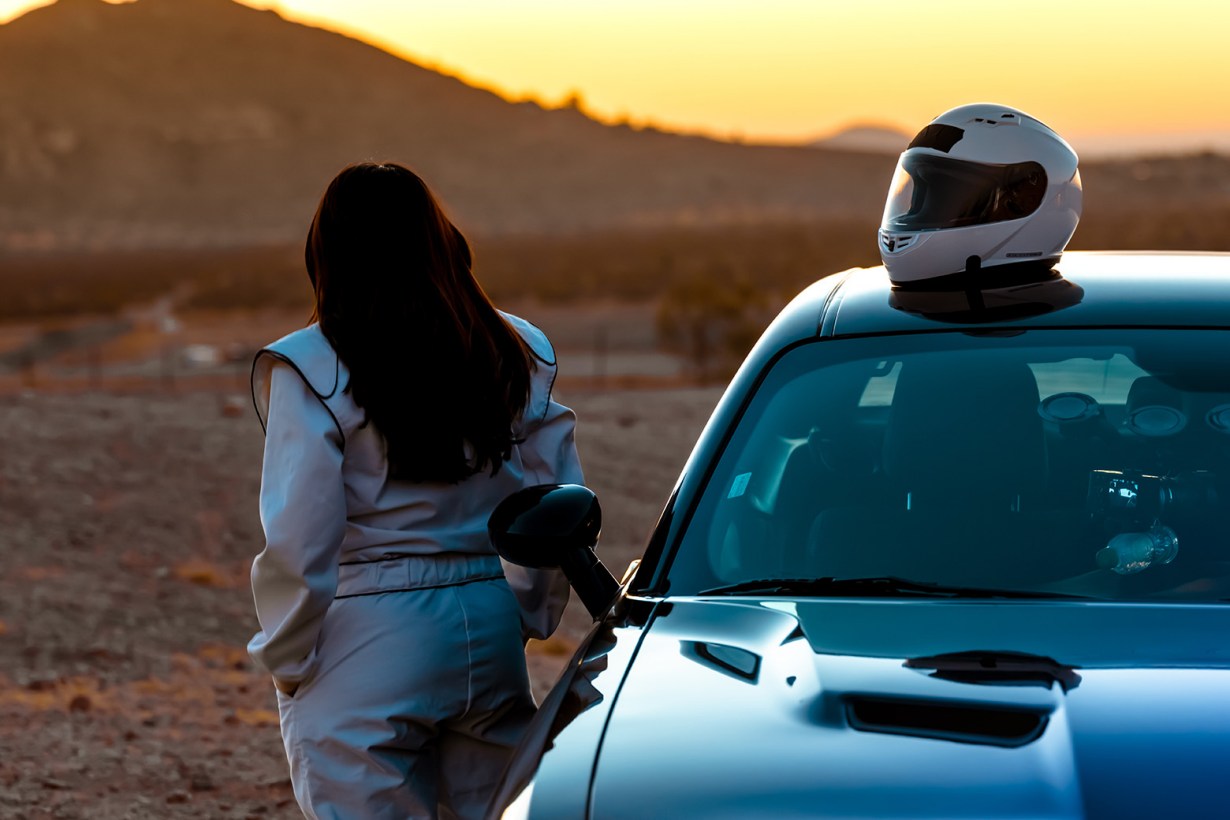 a female race car driver with helmet on top of car