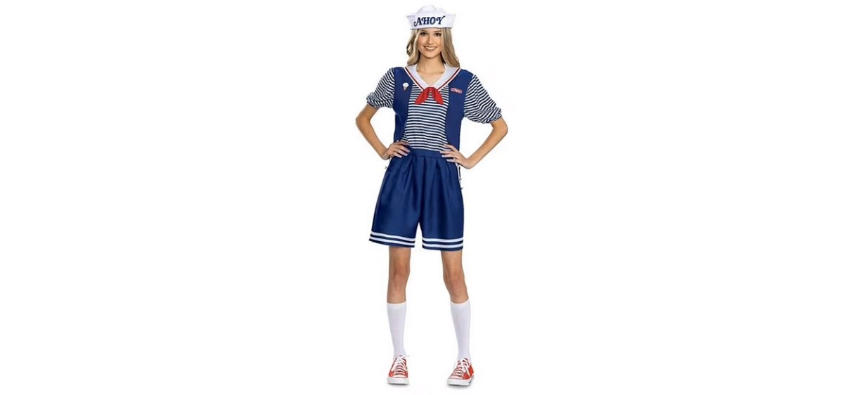 Person wearing blue shorts, a blue and white striped shirt with red necktie, a blue vest and a white sailor hat that says &quot;ahoy.&quot;